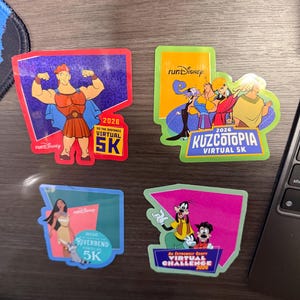 May include: Four rectangular runDisney stickers featuring Hercules with text Go The Distance Virtual 5K 2026, Kuzcotopia Virtual 5K 2026 with characters, Riverbend Virtual 5K 2026 with Pocahontas, and An Extremely Goofy Virtual Challenge 2026 with Goofy and Max.