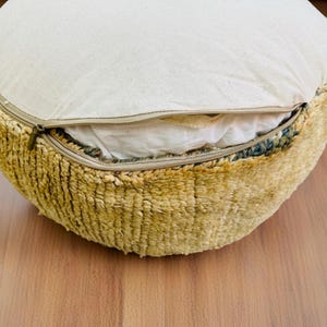 Round Moroccan pouf with a vintage Berber rug pattern in earthy tones, placed on a wooden floor with natural sunlight casting soft shadows.