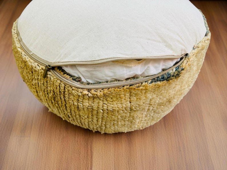 Round Moroccan pouf with a vintage Berber rug pattern in earthy tones, placed on a wooden floor with natural sunlight casting soft shadows.