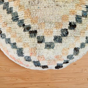 Round Moroccan pouf with a vintage Berber rug pattern in earthy tones, placed on a wooden floor with natural sunlight casting soft shadows.