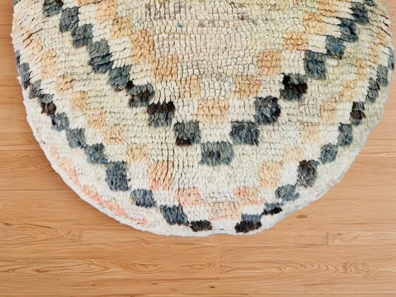 Round Moroccan pouf with a vintage Berber rug pattern in earthy tones, placed on a wooden floor with natural sunlight casting soft shadows.