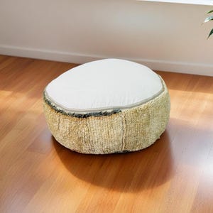 Round Moroccan pouf with a vintage Berber rug pattern in earthy tones, placed on a wooden floor with natural sunlight casting soft shadows.