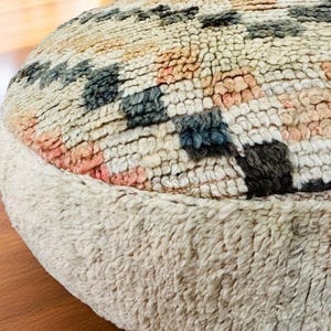 Pu&ograve; includere: Un pouf rotondo e strutturato con base color crema e parte superiore a fantasia. La parte superiore presenta un design geometrico nei toni del crema, rosa, blu e nero. Il pouf &egrave; realizzato in un materiale morbido e tessuto, ideale per un soggiorno o una camera da letto.