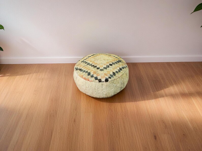Round Moroccan pouf with a vintage Berber rug pattern in earthy tones, placed on a wooden floor with natural sunlight casting soft shadows.