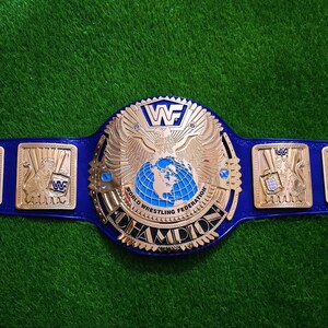 Può includere: Una cintura da campionato in pelle blu con una grande placca centrale dorata raffigurante un'aquila, un globo e la scritta World Wrestling Federation Champion. Due placche laterali dorate più piccole mostrano il logo WWF e figure animali.