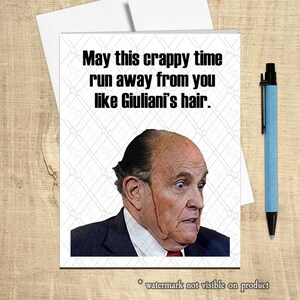 Puede incluir: Una tarjeta de felicitación con el texto "May this crappy time run away from you like Giuliani's hair." presenta una foto de un hombre con expresión de sorpresa. Un bolígrafo azul descansa sobre una superficie de madera.