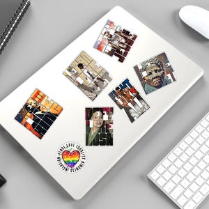 May include: A collection of stickers on a white laptop. The stickers feature portraits and the word "FIGHT" in a mosaic style. A sticker with a rainbow heart and the words "INCLUSION PEACE LOVE EQUALITY KINDNESS" is also present.