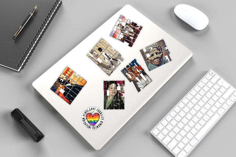 May include: A collection of stickers on a white laptop. The stickers feature portraits and the word "FIGHT" in a mosaic style. A sticker with a rainbow heart and the words "INCLUSION PEACE LOVE EQUALITY KINDNESS" is also present.