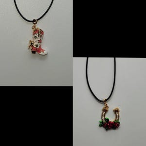 May include: Two necklaces with black cords. One features a gold-toned pendant of a red and white cowboy boot with star details. The other has a gold-toned horseshoe pendant adorned with red roses and green leaves.