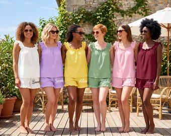May include: Six matching pajama sets consisting of a sleeveless ruffled top and shorts in white, lavender, yellow, sage green, pink, and burgundy. Each pair of shorts features a white cursive name or title printed on the lower right leg hem.