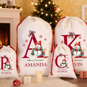 May include: Cream-coloured Christmas gift bags with red drawstrings. Each bag has a snowman design, a letter, and a name. Snowflakes and candy cane accents complete the festive look. Bags are in various sizes.