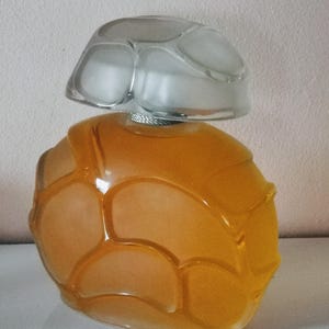Könnte beinhalten: Eine dekorative Parfümflasche mit einzigartigem Design. Die Flasche hat eine warme bernsteinfarbene Farbe mit einem strukturierten, segmentierten Muster. Der klare, mattierte Glasverschluss sitzt oben auf der Flasche. Die Flasche ist wahrscheinlich aus Glas.