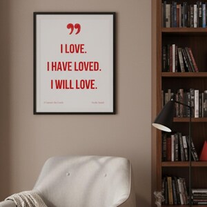 Peut inclure: Une affiche encadrée avec les mots "I LOVE. I HAVE LOVED. I WILL LOVE." en rouge. L'affiche est au-dessus d'un fauteuil crème avec une couverture. Des bibliothèques remplies de livres encadrent le fauteuil. Une petite table d'appoint contient une tasse et des livres.