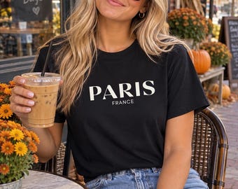 May include: A black short-sleeved crew neck t-shirt featuring the word PARIS in large white capital letters with the word FRANCE printed in smaller white capital letters directly underneath the main text on the front of the garment.