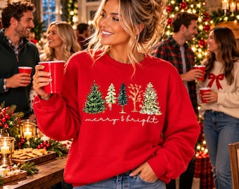 May include: A red long-sleeve sweatshirt featuring a graphic of five stylized Christmas trees in green, white, and gold tones. Below the trees, the text "merry & bright" is printed in a white cursive script font across the chest.