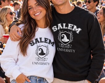 May include: A white sweatshirt and a black sweatshirt, both featuring a graphic print of a shield with a witch hat, the text SALEM UNIVERSITY, and EST. 1626. The white sweatshirt has a black print, while the black sweatshirt has a white print.