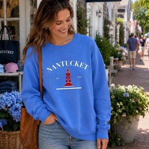 K&ouml;nnte beinhalten: Ein blaues Sweatshirt mit dem Wort "NANTUCKET" in Wei&szlig; &uuml;ber einer rot-wei&szlig;en Leuchtturm-Grafik. Das Sweatshirt hat einen Rundhalsausschnitt und lange &Auml;rmel. Der Text "EST 1686" befindet sich darunter.