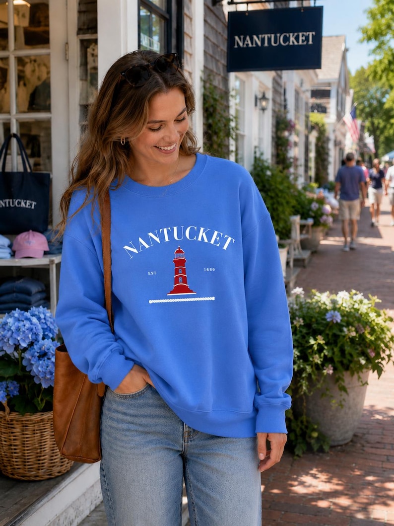 K&ouml;nnte beinhalten: Ein blaues Sweatshirt mit dem Wort "NANTUCKET" in Wei&szlig; &uuml;ber einer rot-wei&szlig;en Leuchtturm-Grafik. Das Sweatshirt hat einen Rundhalsausschnitt und lange &Auml;rmel. Der Text "EST 1686" befindet sich darunter.