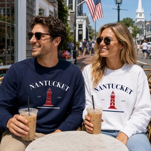 K&ouml;nnte beinhalten: Ein Paar tr&auml;gt passende Sweatshirts mit dem Wort "Nantucket" und einem roten Leuchtturm-Motiv. Die Sweatshirts sind marineblau und wei&szlig;. Sie sitzen an einem Tisch mit Eiskaffee, im Hintergrund eine Stra&szlig;enszene.
