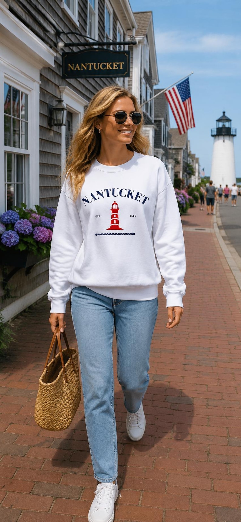 K&ouml;nnte beinhalten: Ein wei&szlig;es Sweatshirt mit dem Wort "Nantucket" in Marineblau, einer roten Leuchtturm-Grafik und dem Jahr "1659". Die Person tr&auml;gt eine hellblaue Jeans, wei&szlig;e Turnschuhe und eine geflochtene Tragetasche.