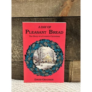 May include: A red book titled "A Day of Pleasant Bread" with the subtitle "The Story of a Country Christmas." The cover features a winter scene inside a blue and green wreath. Author: David Grayson.