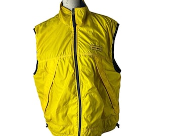 Puede incluir: Chaleco amarillo brillante con ribete negro y cremallera completa. El chaleco tiene un cuello alto y un pequeño parche con el logotipo "POLO SPORT". El chaleco sin mangas parece estar hecho de un material ligero, posiblemente resistente al agua.