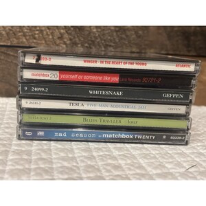 以下が含まれることがあります： さまざまなアルバムタイトルとアーティスト名が記載された6枚のCDのスタック。「Winger - In The Heart Of The Young」、「matchbox twenty - yourself or someone like you」、「Whitesnake」、「Tesla Five Man Acoustical Jam」、「Blues Traveler four」、および「mad season by matchbox twenty」など。
