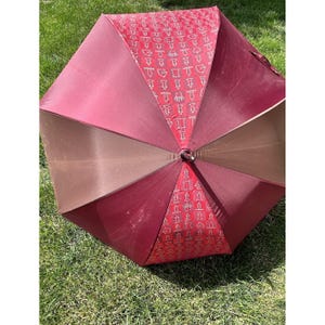 May include: An open umbrella with a burgundy and brown color scheme. The umbrella's panels alternate between solid burgundy and brown, with a patterned burgundy section featuring white designs. The umbrella is resting on green grass.