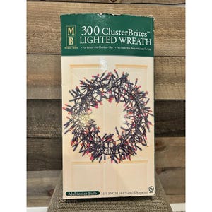 May include: A box for a 300 ClusterBrites lighted wreath. The box features a wreath design with multicolor bulbs. The wreath is 16.5 inches (41.9 cm) in diameter. The box is green and white with the text "MERRY BRITE" and "For Indoor and Outdoor Use".