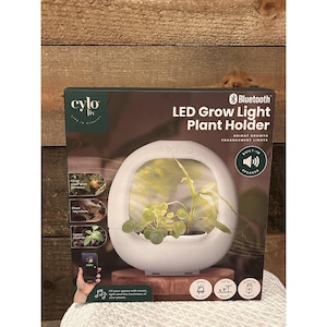 May include: A white LED grow light plant holder with a built-in speaker. The product is in a box with the text "cylo liv" and "LED Grow Light Plant Holder". The box also shows a plant inside the holder and the Bluetooth logo.