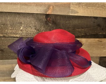 Sombrero formal de paja roja de ala ancha con satén morado y plumas para el Derby de Kentucky.
