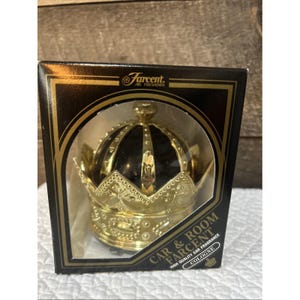 May include: A Farcent brand car and room air freshener in a black box with gold trim. The product is a gold-colored crown-shaped container with a dark interior, visible through a clear plastic window. The text reads Farcent Air Freshener and Cologne.
