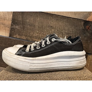 May include: Black canvas low-top sneakers with white laces and a thick, layered white rubber sole. The shoes have a classic design with a modern, chunky sole, suitable for casual wear.