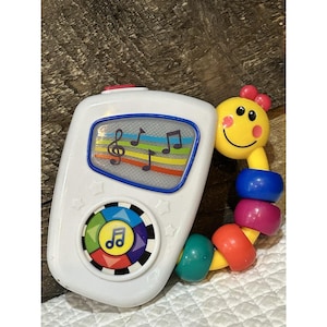 Può includere: Un giocattolo musicale in plastica bianca con uno schermo con note musicali colorate e un tastierino circolare. Sul lato è fissata un'impugnatura gialla a forma di bruco sorridente con perline di plastica blu, viola, arancioni e verdi.