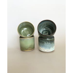Peut inclure: Deux piles de tasses en céramique, chacune avec un émail unique. La pile de gauche est vert clair avec une finition lisse, tandis que celle de droite présente un dégradé de bleu foncé, de sarcelle et de blanc. Chaque ensemble compte deux tasses.