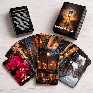 May include: A deck of "Cartes du temps" cards with a black box featuring an hourglass design. The cards are fanned out, displaying various scenic images. The text "Cartes du temps" is visible on the box and some cards. The age range is 14+.