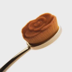 May include: A gold makeup brush with a rose-shaped brush head. The brush head is made of soft, brown bristles.