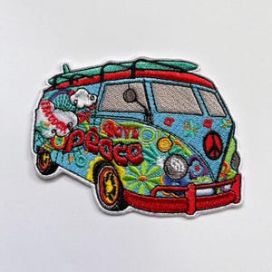 May include: An embroidered patch shaped like a vintage van in light blue, featuring a red bumper, a green surfboard on the roof, and colorful floral patterns. The design includes the word peace in red lettering, white clouds, and a peace sign symbol.