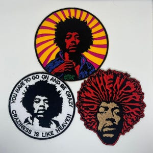 May include: Three embroidered patches featuring a portrait of a musician. One patch has a black afro with a yellow and pink sunburst background. Another is black and white with text. The third patch has red hair.