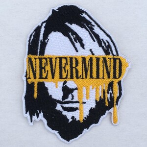 Könnte beinhalten: Gestickter Aufnäher mit einem schwarz-weißen Porträt. Das Wort "NEVERMIND" ist gelb über den Augen, mit gelber Farbe, die heruntertropft. Der Aufnäher hat einen weißen Rand, ideal für Kleidung oder Accessoires.