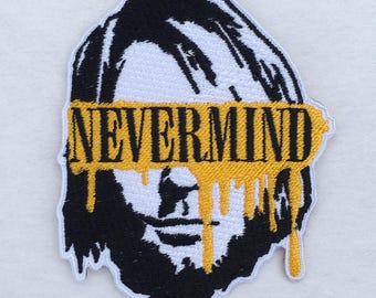 May include: Embroidered patch featuring a black and white portrait with the word "NEVERMIND" in yellow across the eyes. The yellow paint drips down the face, creating a unique design. The patch has a white border.