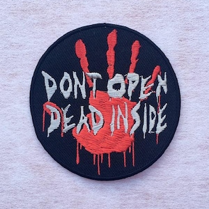 Puede incluir: Un parche bordado circular de color negro con un gráfico de huella de mano roja en el centro. El texto DONT OPEN DEAD INSIDE está bordado en letras blancas sobre la huella, con gotas rojas que se extienden desde las letras y la palma.