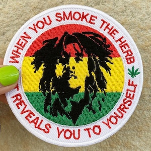 May include: Round embroidered patch with a red, yellow, and green background. The patch features a black silhouette of a person's face and hair. Text in red reads "WHEN YOU SMOKE THE HERB REVEALS YOU TO YOURSELF."