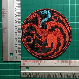 Peut inclure: Écusson noir circulaire représentant un dragon rouge à trois têtes avec un cou bleu. L'écusson est brodé avec des détails complexes. L'écusson mesure environ 7.6 cm de diamètre.