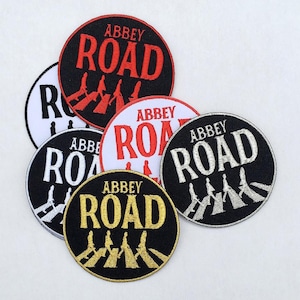 Könnte beinhalten: Runde Aufnäher mit dem Schriftzug "Abbey Road" in verschiedenen Farben wie Rot, Weiß und Gold. Die Aufnäher zeigen eine Illustration von Personen, die einen Zebrastreifen überqueren. Sie sind wahrscheinlich für Kleidung oder Accessoires bestimmt.