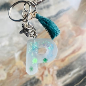 Chaveiro de resina com letra P e trevos de quatro folhas verdes e efeito acetinado. Pingente em formato de abelha e borla. Ideia para presente.