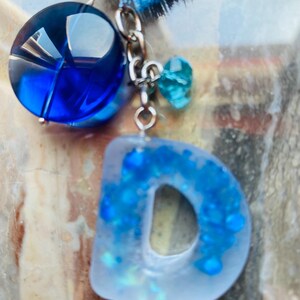 Llavero de resina con la letra D (efecto satinado mate), hecho a mano con borla y dije azules.