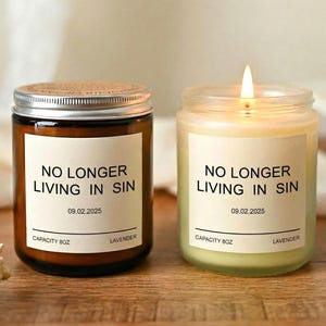 Könnte beinhalten: Zwei Glas-Kerzengläser mit dem Text "NO LONGER LIVING IN SIN" und dem Datum 09.02.2025. Eine Kerze befindet sich in einem dunkelbraunen Glas mit silbernem Deckel, die andere in einem klaren Glas mit einer brennenden Flamme. Beide Kerzen sind mit "CAPACITY 8OZ" und "LAVENDER" beschriftet.