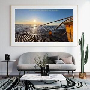 Könnte beinhalten: Gerahmtes Foto einer Strandlandschaft bei Sonnenuntergang. Das Bild zeigt ein Boot, Seile und eine gelbe Boje im nassen Sand. Der Himmel ist ein Farbverlauf aus Orange und Blau. Deutscher Text ist oben sichtbar.