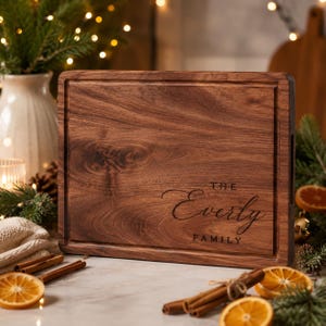 Könnte beinhalten: Ein rechteckiges, dunkelbraunes Holzschneidebrett mit einer gerillten Kante und dem eingravierten Text "THE Everly FAMILY" auf der Vorderseite. Das Brett weist eine sichtbare Holzmaserung und eine glatte Oberfläche in einem natürlichen Holzton auf.